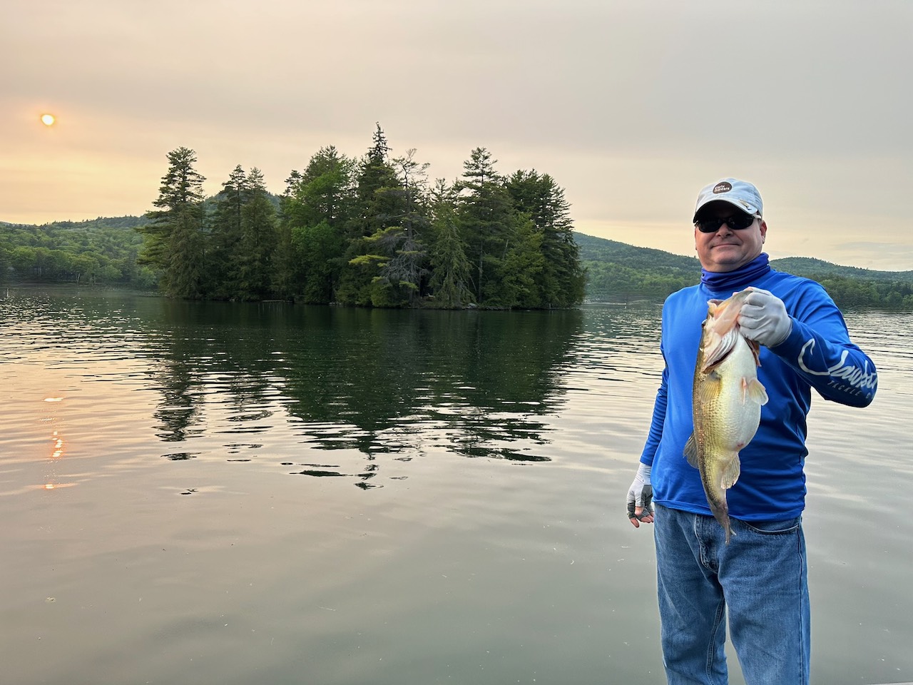 Brian Barde, founder of Kindlewood Cares, holding a largemouth bass on a lake at sunrise